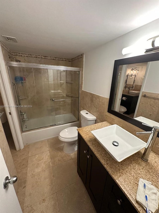 full bathroom with toilet, tile patterned flooring, vanity, bath / shower combo with glass door, and tile walls