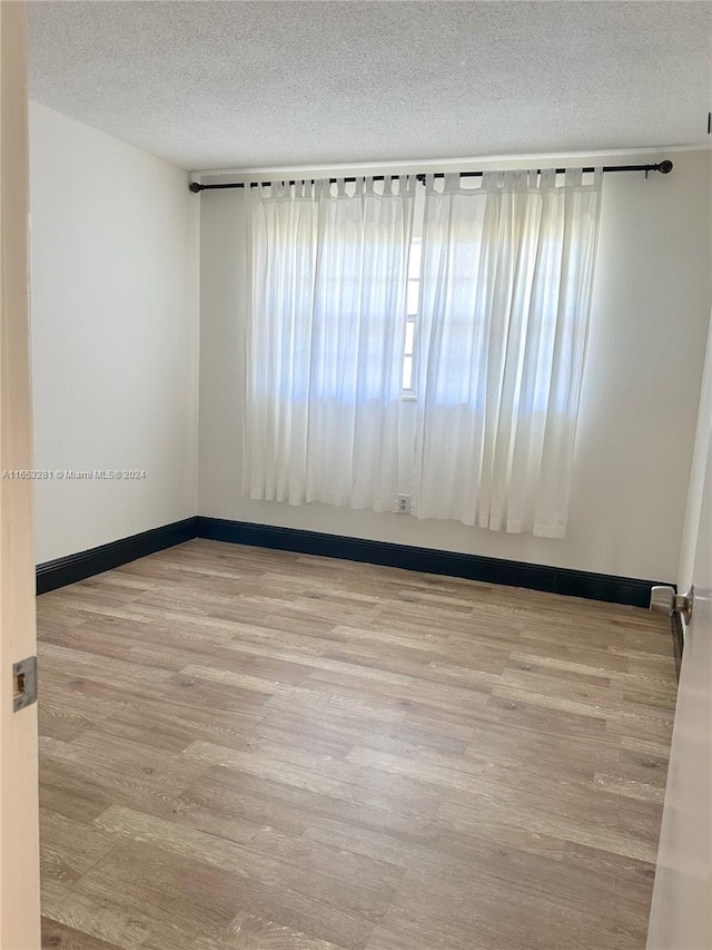 spare room with a textured ceiling and light wood-type flooring