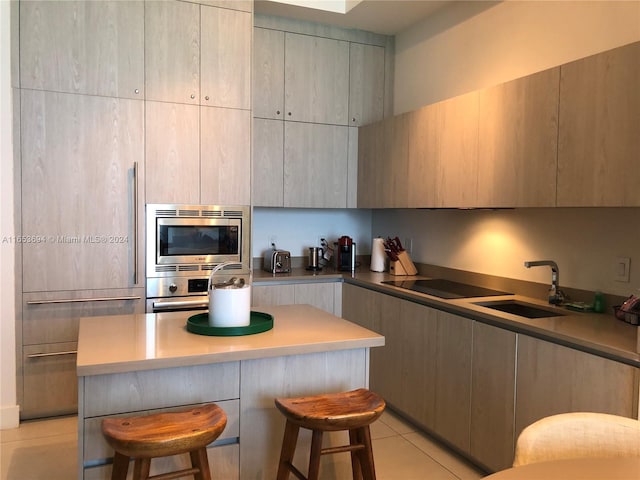 kitchen featuring light tile patterned floors, stainless steel appliances, sink, a breakfast bar area, and a kitchen island