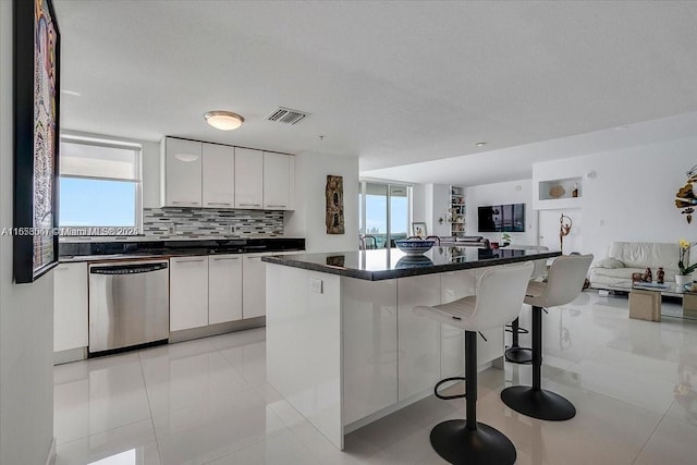 kitchen featuring a kitchen island, light tile patterned floors, dishwasher, white cabinetry, and a breakfast bar area