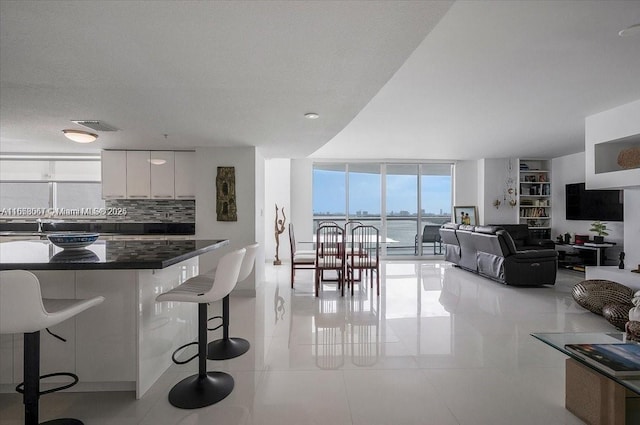 kitchen with light tile patterned floors, a wall of windows, tasteful backsplash, a kitchen bar, and white cabinets