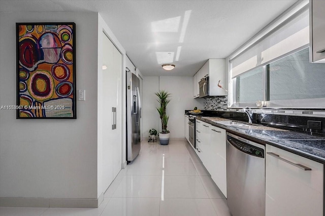 kitchen featuring backsplash, sink, appliances with stainless steel finishes, light tile patterned flooring, and white cabinetry