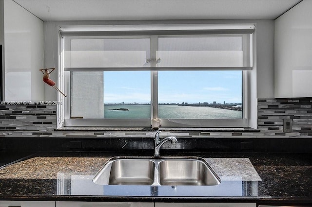 kitchen with backsplash, dark stone countertops, sink, and a water view