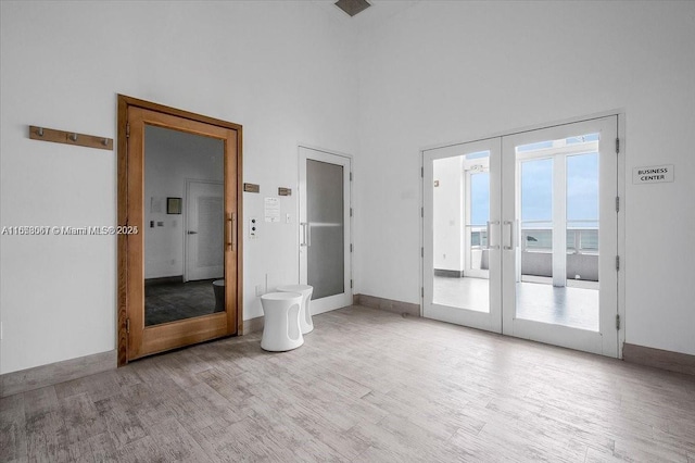 spare room featuring french doors, light hardwood / wood-style floors, and a high ceiling