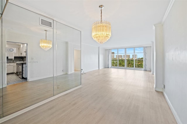 empty room featuring a wall of windows, light hardwood / wood-style flooring, crown molding, and a notable chandelier