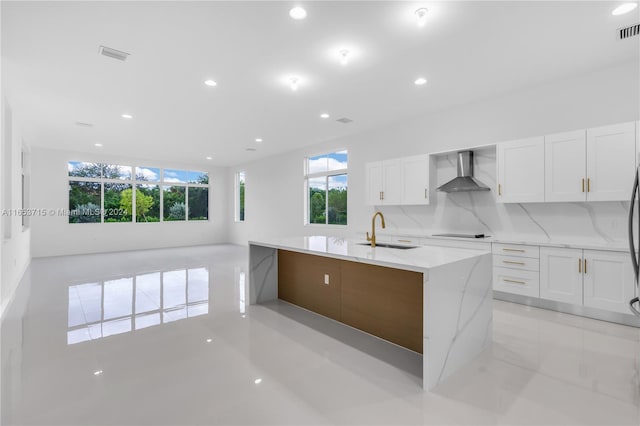 kitchen with electric stovetop, white cabinetry, sink, light stone countertops, and wall chimney range hood