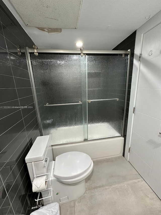 bathroom with a textured ceiling, toilet, and bath / shower combo with glass door