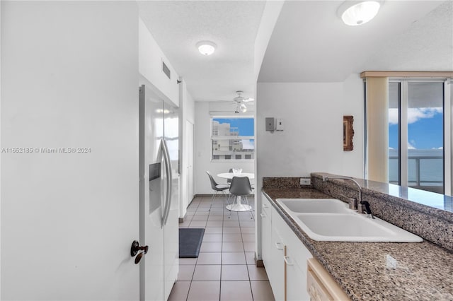 kitchen with white cabinetry, sink, ceiling fan, stainless steel fridge, and a water view