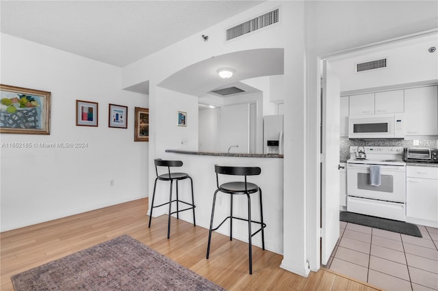 kitchen featuring white cabinets, light wood-type flooring, white appliances, and tasteful backsplash