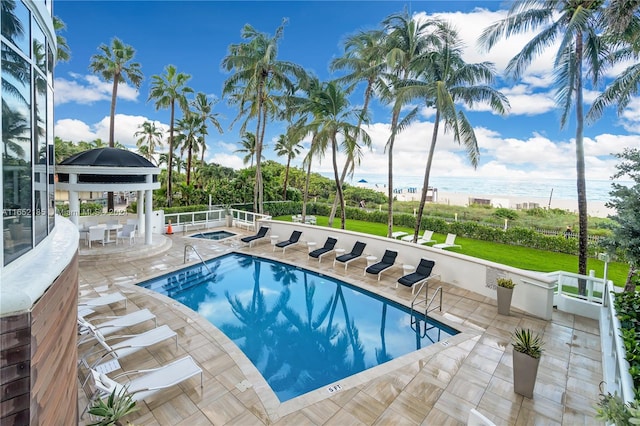 view of swimming pool with a patio area, a water view, and a hot tub