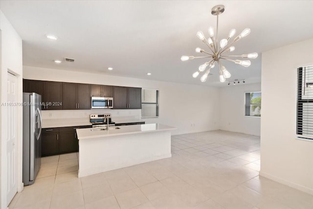 kitchen with a chandelier, dark brown cabinets, a center island with sink, stainless steel appliances, and light tile patterned floors