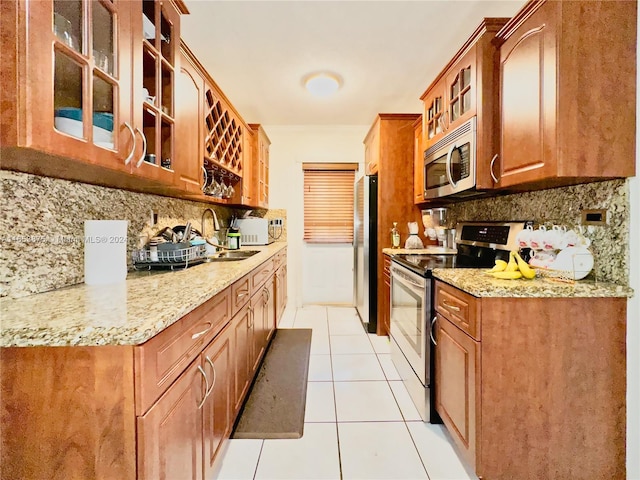 kitchen with light tile patterned floors, appliances with stainless steel finishes, tasteful backsplash, sink, and light stone counters