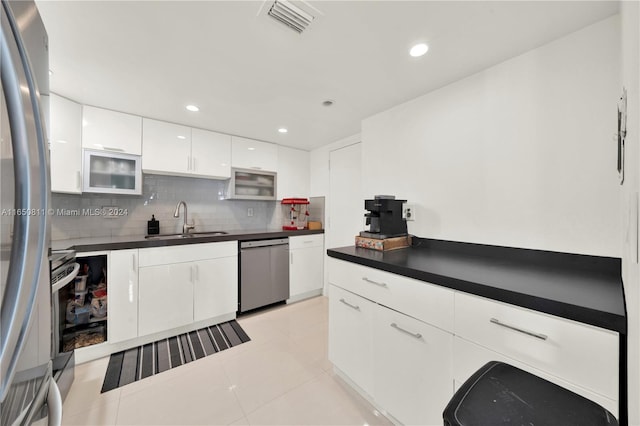 kitchen featuring light tile patterned floors, tasteful backsplash, stainless steel dishwasher, sink, and white cabinetry