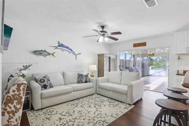 living room with a textured ceiling, ceiling fan, and dark hardwood / wood-style floors