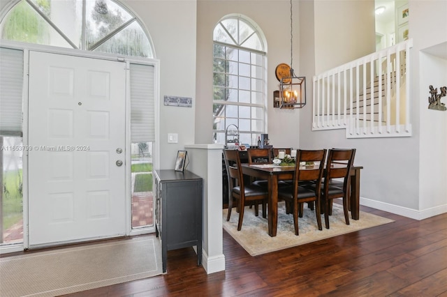 dining space with a healthy amount of sunlight, dark hardwood / wood-style floors, a towering ceiling, and a notable chandelier