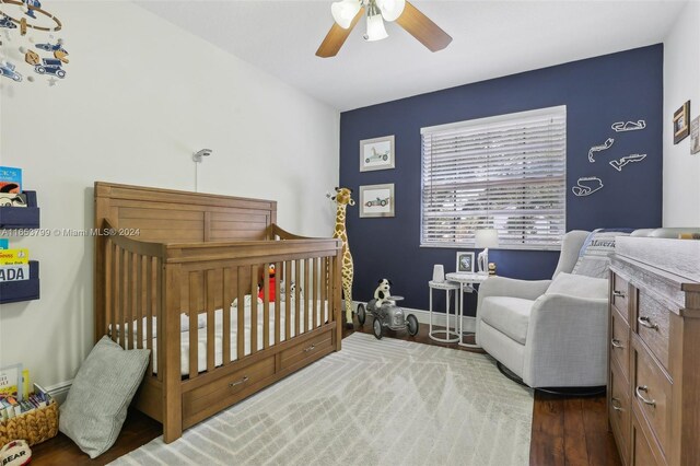 bedroom featuring ceiling fan, dark hardwood / wood-style flooring, and a crib