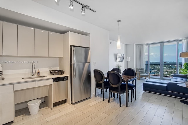 kitchen featuring white cabinets, hanging light fixtures, a wall of windows, appliances with stainless steel finishes, and sink