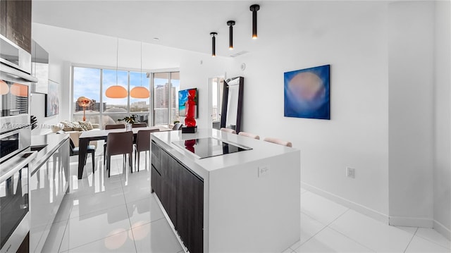 kitchen with a kitchen island, oven, decorative light fixtures, dark brown cabinets, and light tile patterned floors