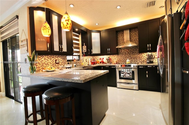 kitchen featuring a textured ceiling, decorative light fixtures, kitchen peninsula, appliances with stainless steel finishes, and wall chimney range hood