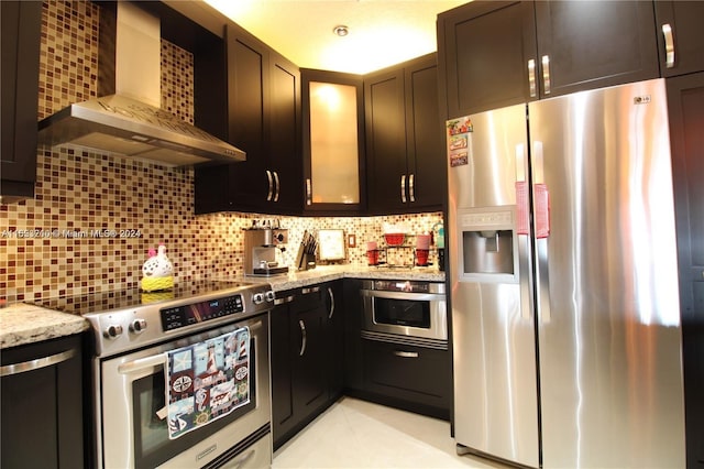 kitchen featuring dark brown cabinets, stainless steel appliances, light stone countertops, decorative backsplash, and wall chimney exhaust hood