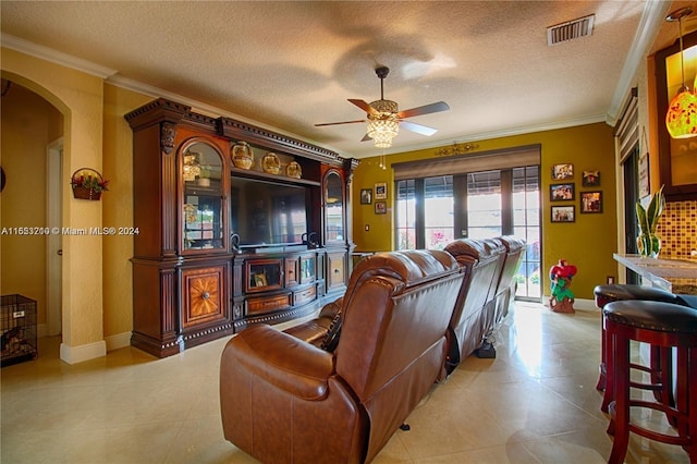 living room featuring light tile patterned flooring, ceiling fan, crown molding, and a textured ceiling