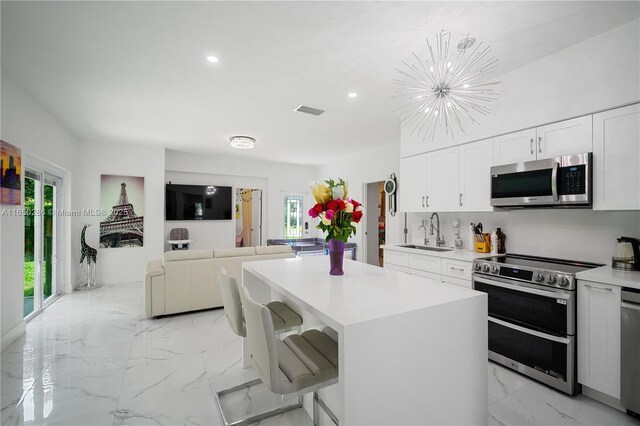 kitchen featuring appliances with stainless steel finishes, white cabinets, a kitchen island, a breakfast bar area, and sink