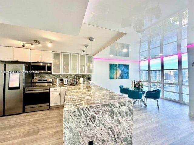 kitchen featuring light stone countertops, light hardwood / wood-style flooring, appliances with stainless steel finishes, tasteful backsplash, and white cabinetry