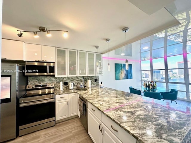 kitchen with light hardwood / wood-style flooring, light stone counters, stainless steel appliances, white cabinetry, and tasteful backsplash