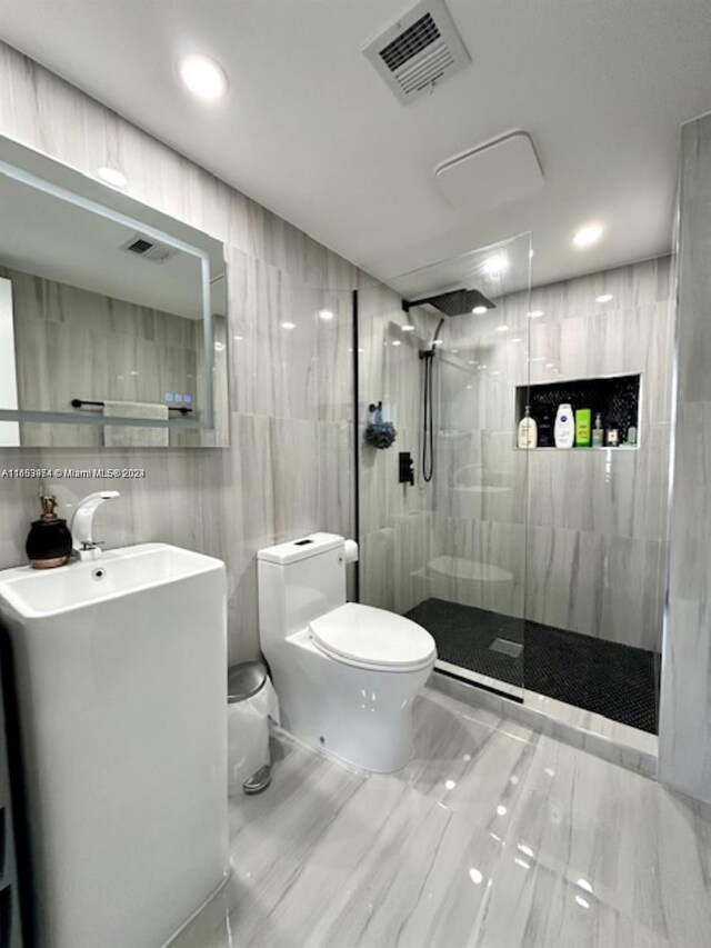 bathroom with vanity, toilet, a tile shower, and tile walls