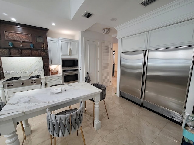 kitchen with dark brown cabinetry, built in appliances, light stone counters, and white cabinetry