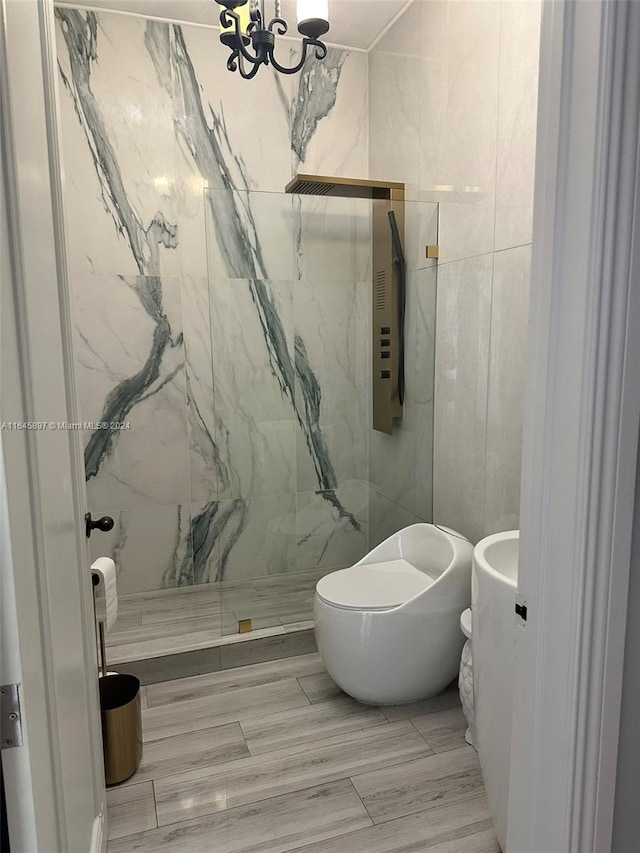 bathroom featuring a tile shower, hardwood / wood-style floors, tile walls, an inviting chandelier, and toilet