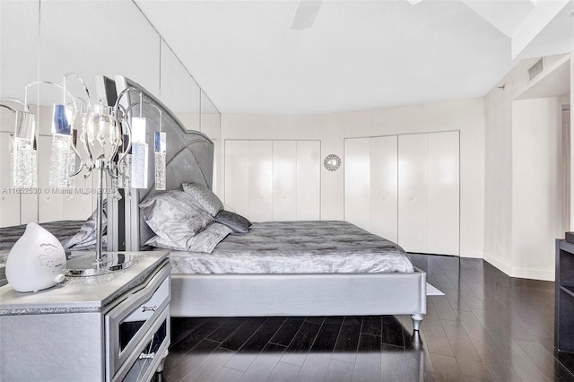 bedroom featuring dark wood-type flooring, ceiling fan, and multiple closets