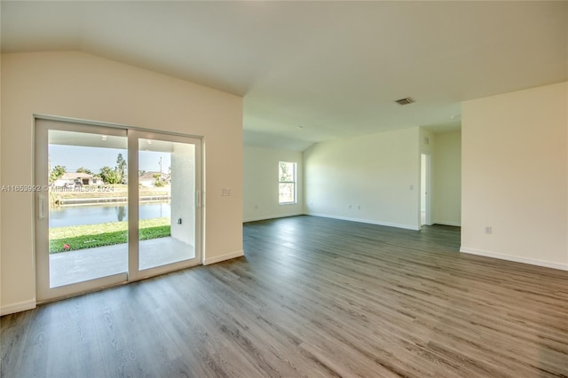 empty room featuring lofted ceiling, plenty of natural light, wood-type flooring, and a water view