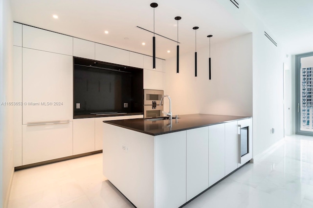 kitchen with a kitchen island with sink, hanging light fixtures, sink, and white cabinetry