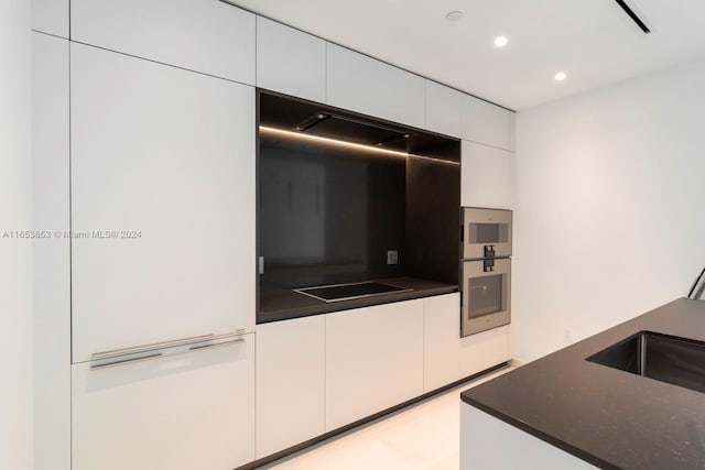 kitchen with dark stone counters, white cabinets, stainless steel double oven, and black electric cooktop