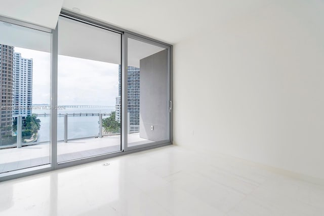 unfurnished room featuring a wall of windows, a water view, and tile patterned floors