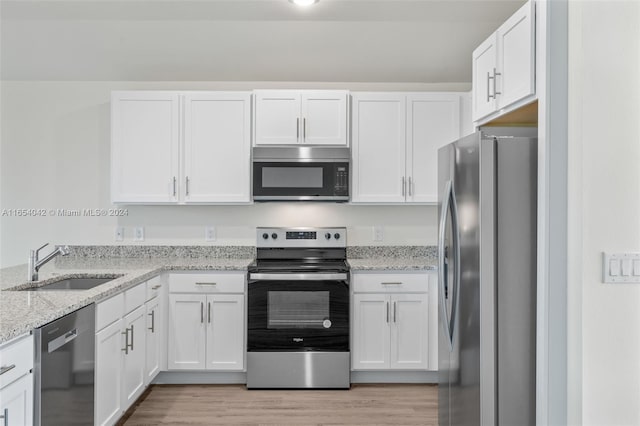 kitchen with stainless steel appliances, light stone counters, light wood-type flooring, and white cabinetry