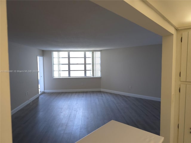 empty room featuring baseboards and dark wood-style flooring