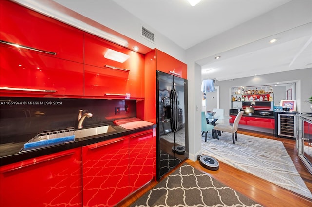 kitchen with black refrigerator with ice dispenser, beverage cooler, and hardwood / wood-style flooring