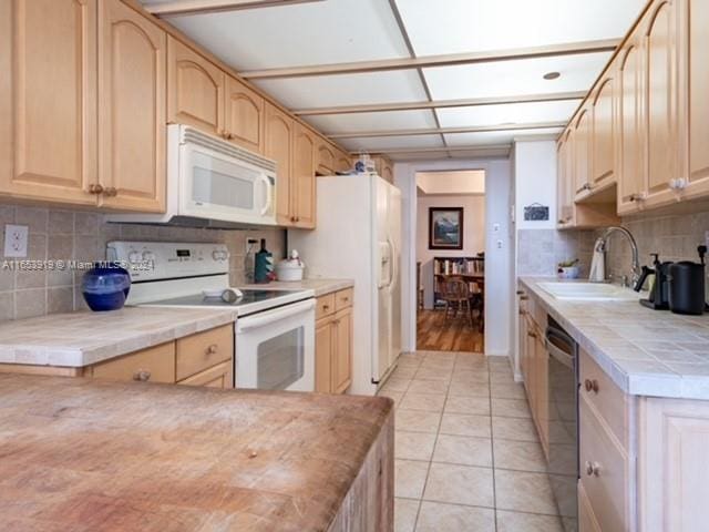 kitchen with white appliances, light tile patterned floors, light brown cabinetry, sink, and decorative backsplash