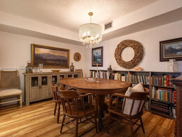 dining room featuring a textured ceiling, a notable chandelier, and light hardwood / wood-style floors