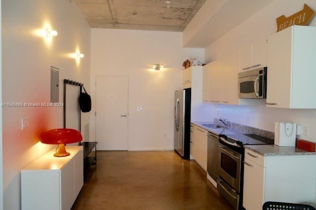 kitchen with concrete floors, appliances with stainless steel finishes, electric panel, white cabinetry, and sink