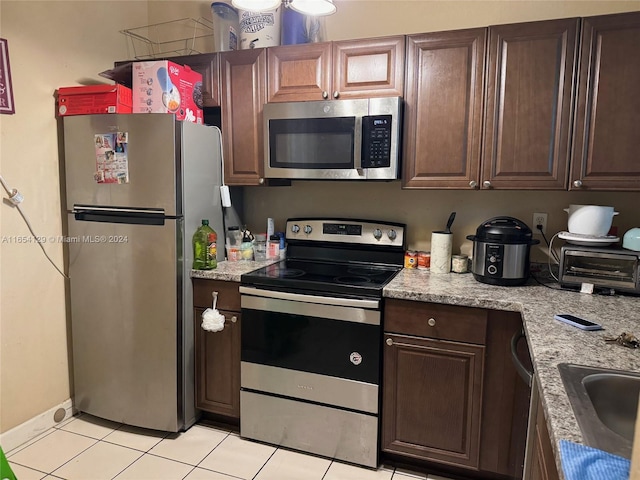 kitchen with appliances with stainless steel finishes, light stone counters, light tile patterned floors, and sink