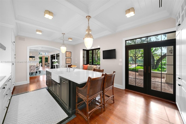 kitchen with a kitchen island with sink, light hardwood / wood-style flooring, french doors, decorative light fixtures, and coffered ceiling