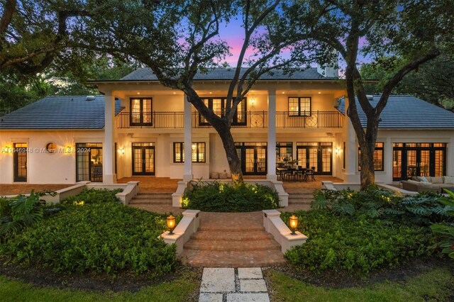 back house at dusk featuring french doors and a balcony