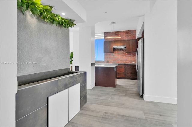 kitchen with stainless steel fridge, a kitchen island, light hardwood / wood-style floors, and brick wall