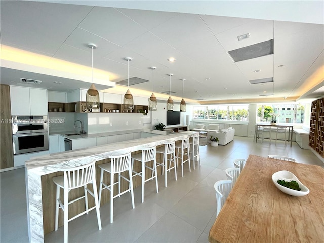 kitchen with hanging light fixtures, stainless steel double oven, sink, a breakfast bar, and white cabinets