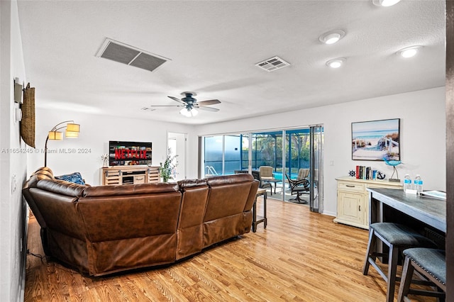 living room featuring ceiling fan, light hardwood / wood-style floors, and a textured ceiling