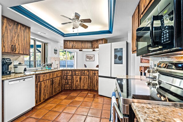 kitchen with white appliances, sink, ceiling fan, decorative backsplash, and a tray ceiling