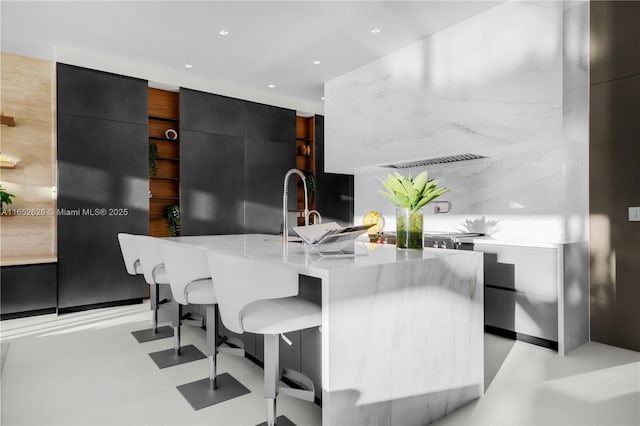 kitchen with a center island with sink, a kitchen breakfast bar, and light stone counters